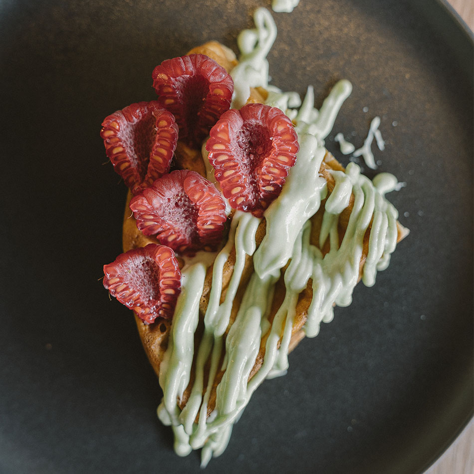 Gaufre ronde au matcha et à la framboise, posée sur une assiette noire